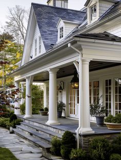 a white house with large columns and pillars on the front porch, surrounded by greenery