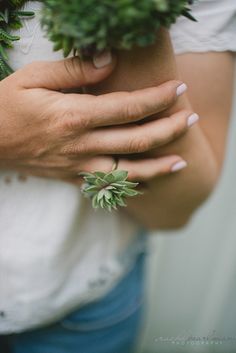 a close up of a person's hands holding plants and wearing a white shirt