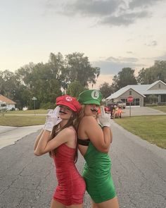 two women in green and red dresses are standing on the side of the road with their arms around each other