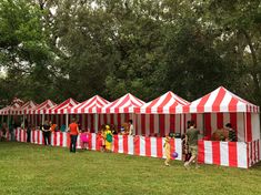 several people are standing in front of red and white striped tents on the grass near trees