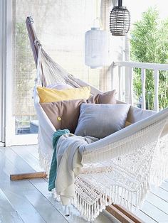 a white hammock with pillows and blankets on the outside porch in front of a window