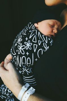 a woman holding a baby wrapped in a black and white wrap around her neck with the word nola written on it