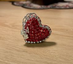 a red heart shaped brooch sitting on top of a wooden table next to a rug