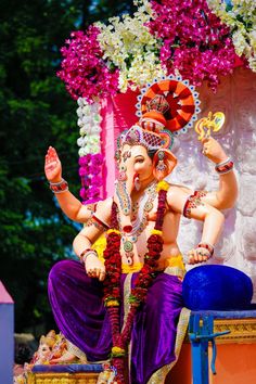 a statue of the god ganesh in front of a flowered wall and trees