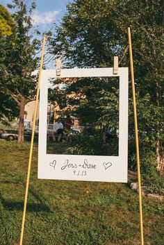 a white sign sitting on top of a lush green field next to a tree filled park