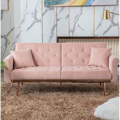 a pink couch sitting on top of a rug in a living room next to a painting