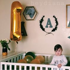 a baby sitting in a crib with balloons and decorations on the wall behind him