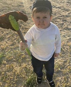 a little boy holding a baseball bat on top of a sandy beach next to a teddy bear