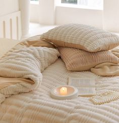 a bed with two pillows and a candle on top of it next to an open book