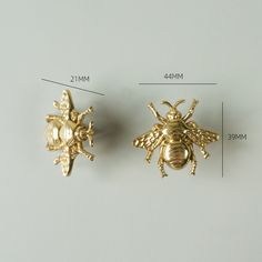 two gold bee brooches sitting next to each other