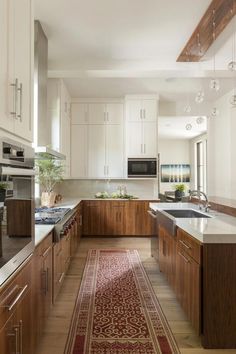 a large kitchen with white cabinets and wooden flooring, along with a red runner rug