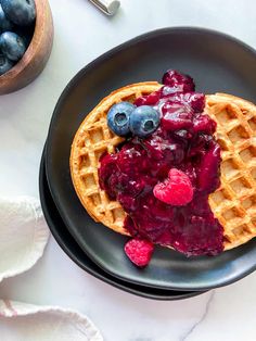 a waffle topped with blueberries and raspberry sauce on a black plate