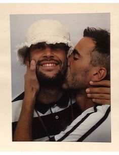 two men are kissing each other while one is wearing a white hat and the other has a black and white striped shirt