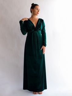 a woman in a long green dress standing against a white wall with her hands on her hips