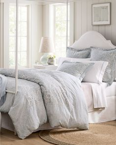 a white bed sitting in a bedroom next to a window covered in pillows and blankets