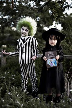 two children dressed up in halloween costumes standing next to each other, one holding a sign