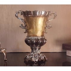 a silver vase sitting on top of a table next to a stack of books and a chair