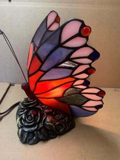 a colorful glass butterfly lamp sitting on top of a white table next to a light bulb