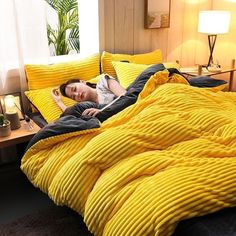 a woman laying on top of a bed covered in yellow comforter and pillows, next to a night stand