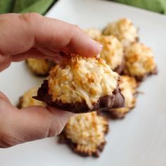 a hand holding a chocolate covered cookie on top of a white plate with other cookies in the background