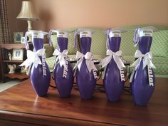 six purple bowling pins with white ribbons tied around them sitting on a table in front of a couch