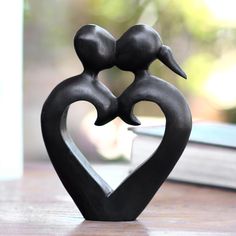 a black sculpture with two birds in the shape of a heart on top of a table