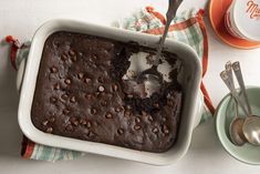 a chocolate cake in a white baking dish with spoons on the table next to it