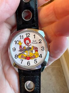 Awesome excellent condition (only worn a few times) Ronald McDonald's wristwatch, from 1976. The face shows a waving old school Ronald McDonald and the words "Swiss Made 17 Jewels." Tiny scratch across glass (pictured), barely noticeable when worn. The silver face and black leather watch are like new. The strap features 6 decorative holes in additional to the adjustable hole closure. Not sure if the watch works-- I'm sure it does, but I make no guarantees! A fabulous collector piece. Retro Analog-style Collectible Watch Accessories, Retro Automatic Collectible Watches, Retro Watch Accessories With Subdials, Black Leather Watch, Retro Watches, Chip Bags, Glass Pictures, Wristwatch Men, Swiss Made