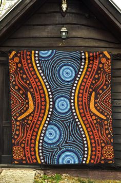 a quilt hanging on the side of a wooden building in front of a tree and grass