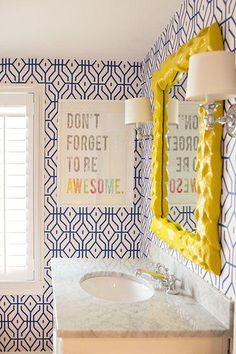 a bathroom with blue and white wallpaper has a sink, mirror, and window