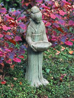 a statue in the middle of a garden with purple and red leaves behind it,