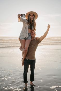 a man carrying a woman on his back at the beach while she holds her up in the air