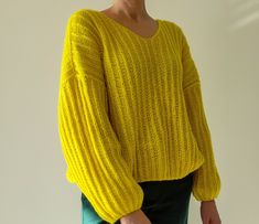 a woman wearing a yellow sweater and green pants standing in front of a white wall