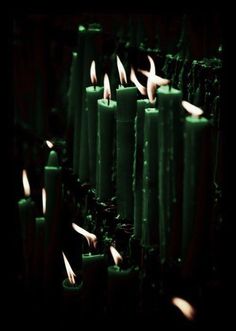 many lit candles are lined up in a row with one candle glowing green and the other white