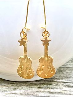 These are such fun music themed earrings. Little golden brass guitar charms and star charms hang from simple gold plate ear wires. Each earring measures approx. 2  inches from the top of the ear wire to the bottom of the charm.   A whimsical gift for the guitarist or music lover!  Your earrings will arrive in a beige cotton drawstring bag with a gift tag. Perfect for gift giving or a fun little treat for yourself. This jewelry bag can be re-purposed to hold your jewelry while traveling, use it in your purse as a makeup bag or you can put some lavender in it and it becomes a nice smelling sachet. PLEASE NOTE: ►There are NO returns on earrings (for health/hygiene reasons) See more jewelry and vintage treasures here: http://www.etsy.com/shop/redtruckdesigns And stop by my other shop to see my Guitar Earrings, Western Music, Fun Music, Whimsical Gifts, Music Jewelry, Rock N’roll, Cotton Drawstring Bags, Music Themed, Jewelry Bag