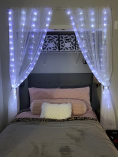 a bed that has some lights on the headboard and curtains over it in a bedroom