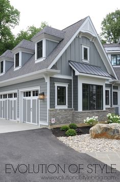 a large gray house with white trim and windows on the front, surrounded by rocks