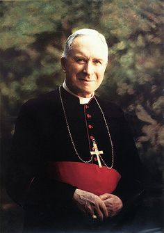 an older man wearing a priest's outfit and holding a red book