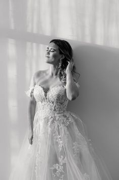 a woman in a wedding dress leaning against a wall with her hand on her head