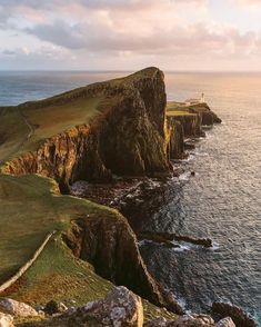 an aerial view of the ocean and cliffs at sunset, with a lighthouse in the distance