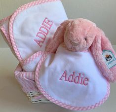 a pink stuffed bunny sitting in a basket with personalized bibs on it's back