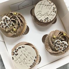 three decorated cupcakes sitting in a box on a marble counter top with the words happy birthday written on them