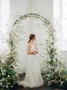 a woman in a white dress standing under an arch of flowers