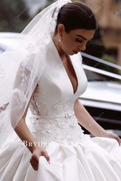 a woman in a white wedding dress and veil walking down the street with her hand on her hip