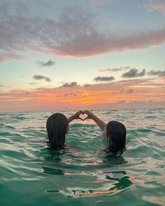 two people in the water making a heart shape with their hands while the sun sets