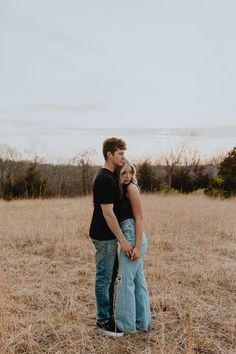 a man and woman standing in the middle of an open field with their arms around each other