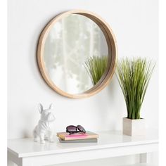 a white table topped with a mirror and a vase filled with grass next to a book