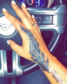 a woman's hand on the steering wheel of a car with a feather tattoo