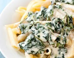 a white plate topped with pasta covered in cheese and spinach sauce on top of it