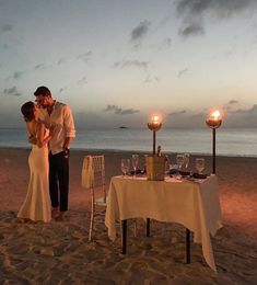 a man and woman standing on top of a beach next to a table covered in candles